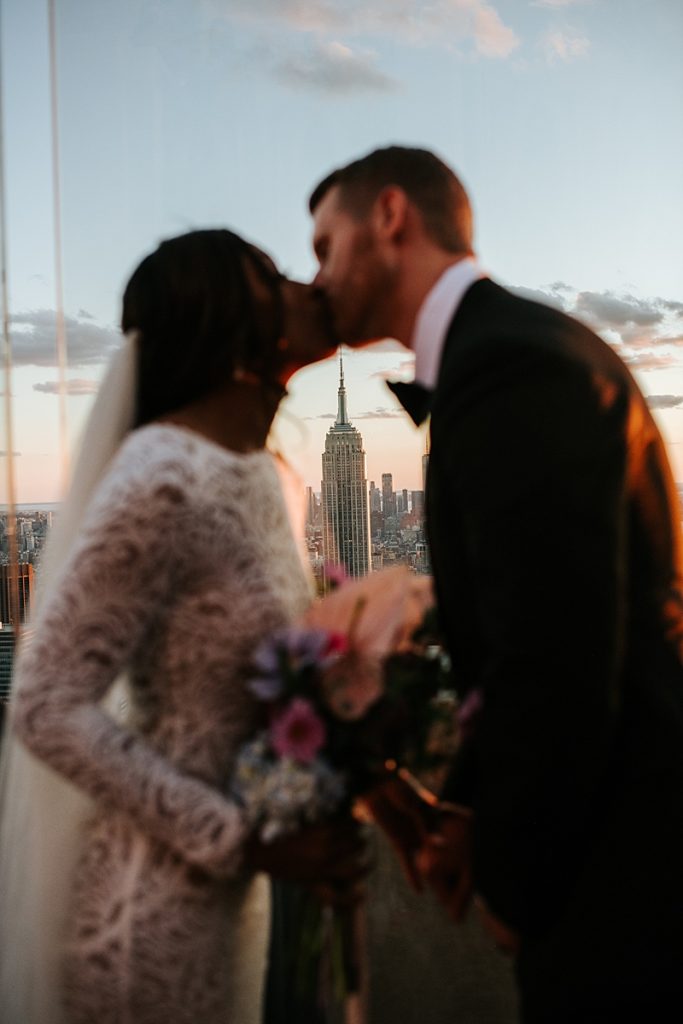 Couple gets married at Top of the Rock with the Empire State Building glowing in the setting sun behind them.