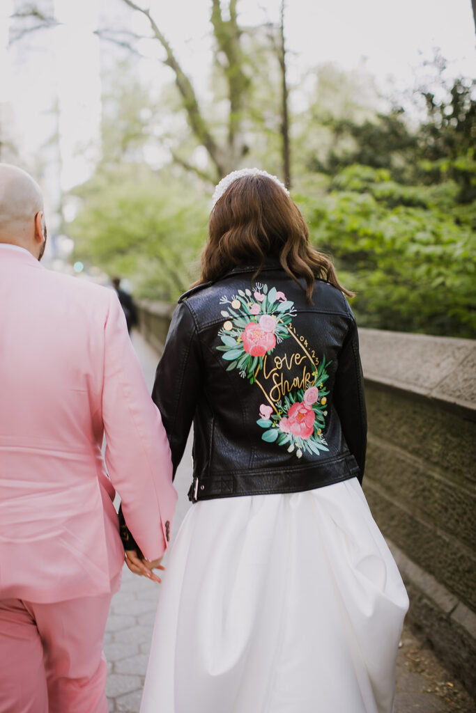 NYC elopement bride wears gorgeous white dress and leather jacket with pink embroidered flowers.