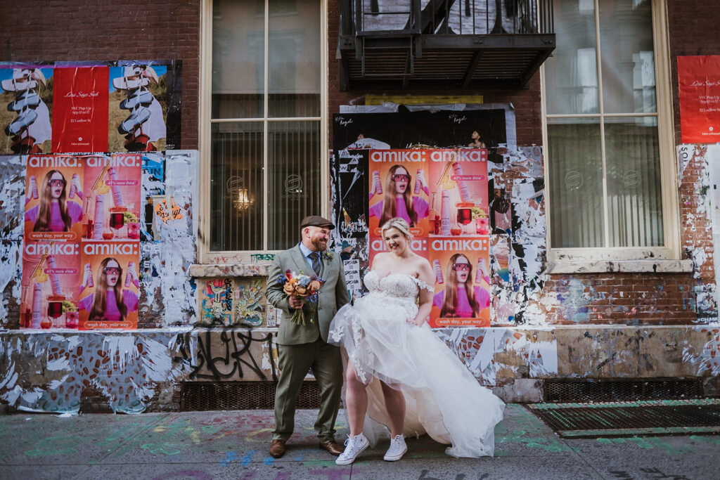 Stylish elopement bride rocks lace and tulle dress with Converse sneakers. She is standing with her husband in front of a graffiti wall in NYC.
