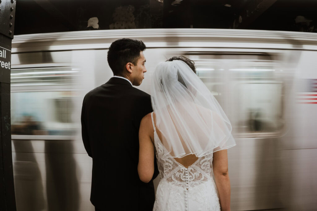 Couple elopes in NYC and waits for the subway in wedding dress.