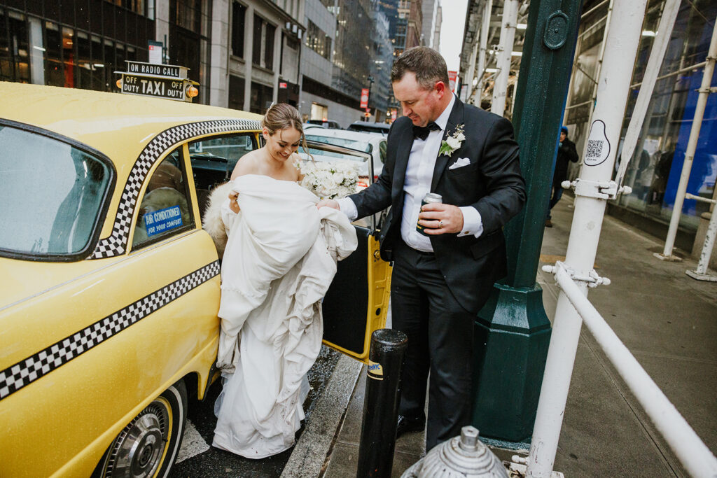 Husband helps wife out of their vintage NYC taxi on their wedding day.